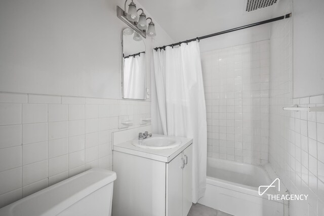 full bathroom with vanity, tile walls, shower / tub combo with curtain, and toilet