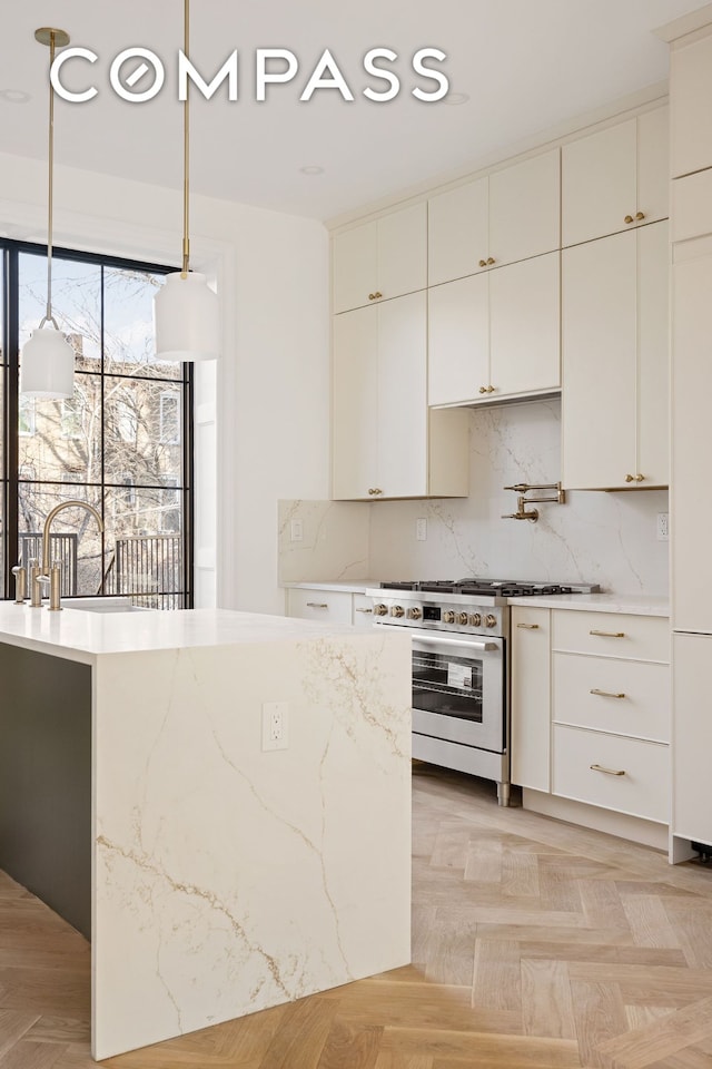 kitchen with pendant lighting, stainless steel range, light stone counters, white cabinets, and decorative backsplash