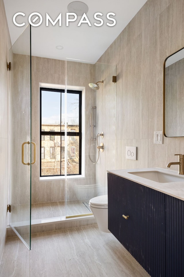 full bathroom with a shower stall, tile walls, vanity, and toilet