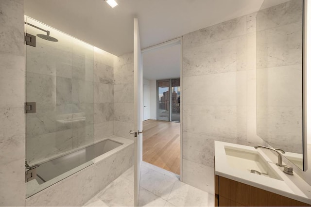 bathroom featuring tile patterned floors, vanity, combined bath / shower with glass door, and tile walls