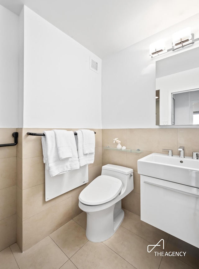 bathroom featuring wainscoting, toilet, tile patterned flooring, vanity, and tile walls