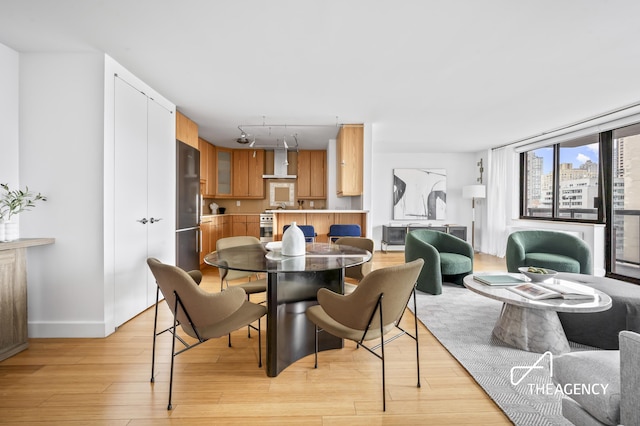 dining space featuring rail lighting, light wood-style flooring, and baseboards