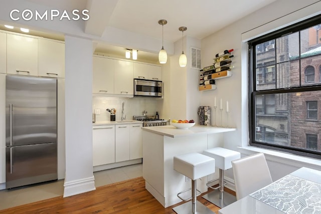 kitchen featuring a breakfast bar, decorative light fixtures, kitchen peninsula, stainless steel appliances, and white cabinets