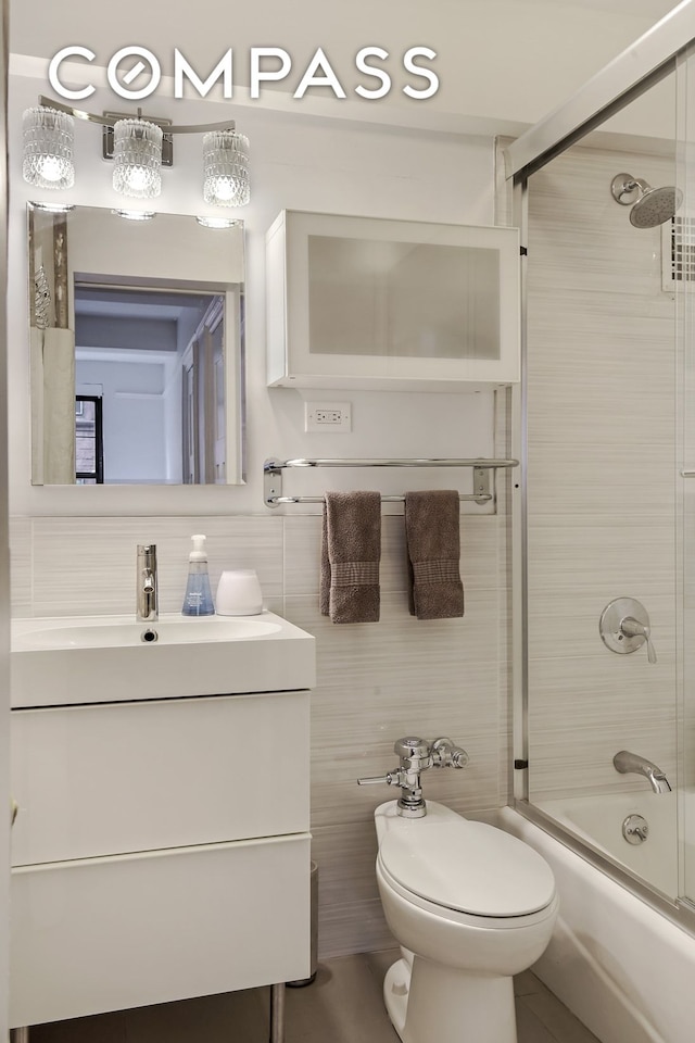 full bath featuring combined bath / shower with glass door, toilet, tile walls, and vanity