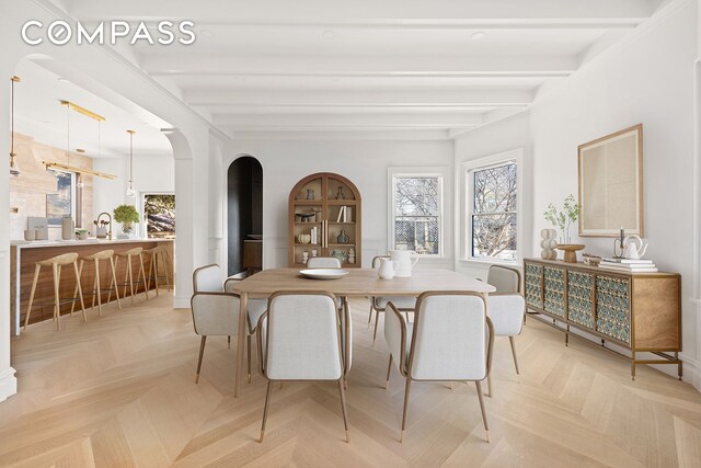 dining area with arched walkways and beamed ceiling