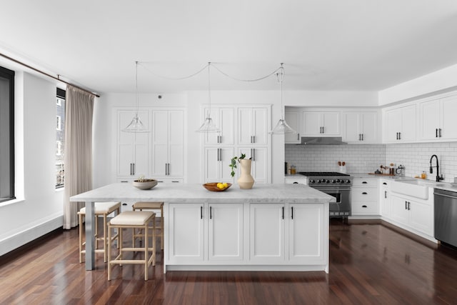 kitchen featuring under cabinet range hood, stainless steel appliances, a kitchen island, a sink, and white cabinets