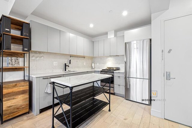 kitchen with light wood finished floors, backsplash, light countertops, gray cabinets, and stainless steel appliances