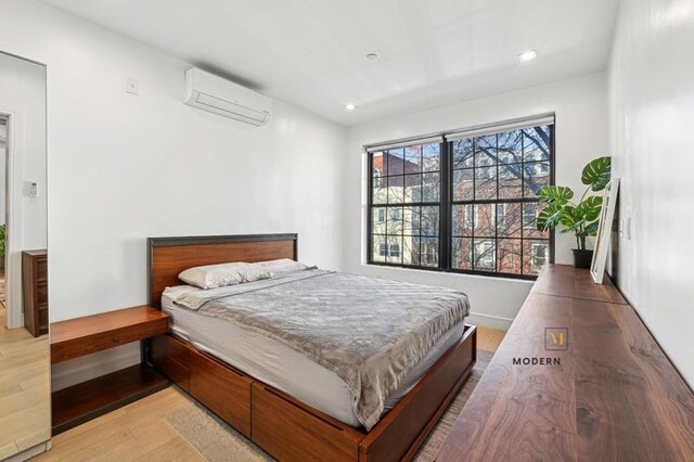 bedroom with a wall unit AC, recessed lighting, and light wood-type flooring