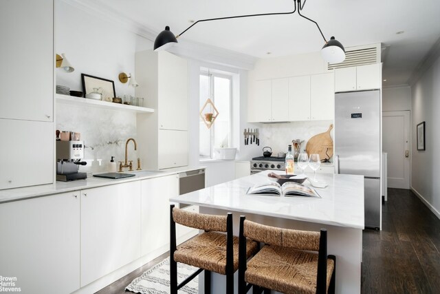 kitchen with white cabinetry, sink, a breakfast bar area, stainless steel built in fridge, and dark wood-type flooring