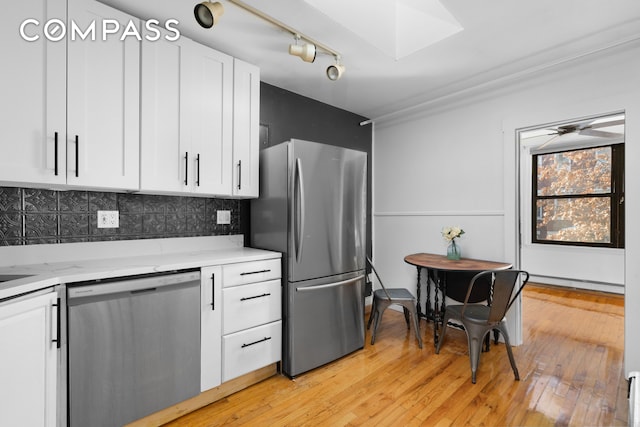 kitchen featuring decorative backsplash, light wood-style flooring, a skylight, stainless steel appliances, and white cabinetry