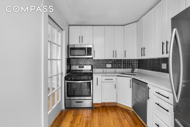 kitchen with decorative backsplash, appliances with stainless steel finishes, wood finished floors, white cabinetry, and a sink