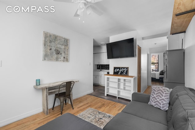 living room with a ceiling fan, light wood-style floors, and baseboards