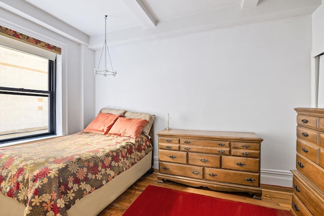 bedroom with wood finished floors, beam ceiling, and baseboards