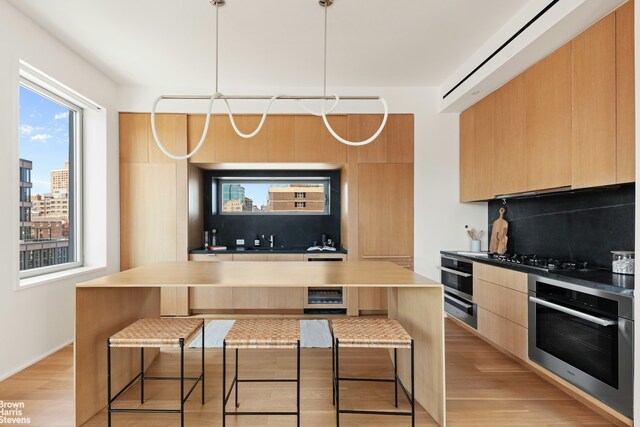 kitchen with hanging light fixtures, a breakfast bar area, oven, and light wood-type flooring