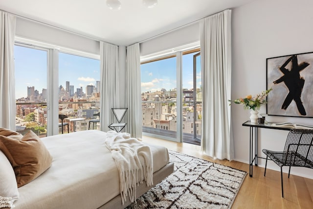 bedroom featuring access to exterior, wood finished floors, a city view, and multiple windows