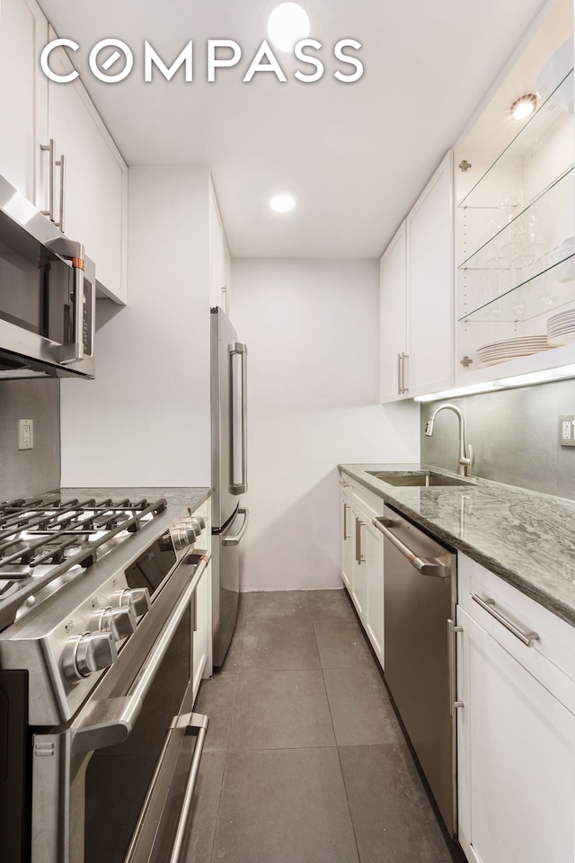 kitchen with dark tile patterned flooring, white cabinets, appliances with stainless steel finishes, and a sink