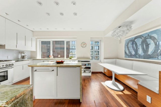 kitchen with hardwood / wood-style floors, white cabinetry, stove, a center island, and light stone counters