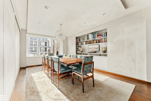 dining area with built in features, light hardwood / wood-style floors, and a chandelier