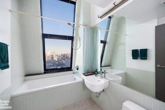 bathroom with tile walls, sink, toilet, and tiled tub