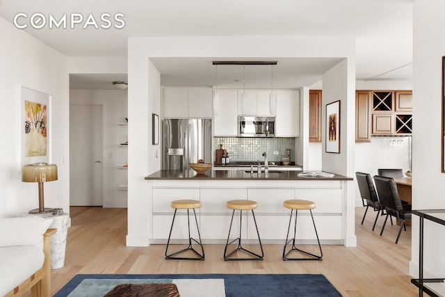 kitchen with dark countertops, a breakfast bar area, light wood-type flooring, stainless steel appliances, and a sink