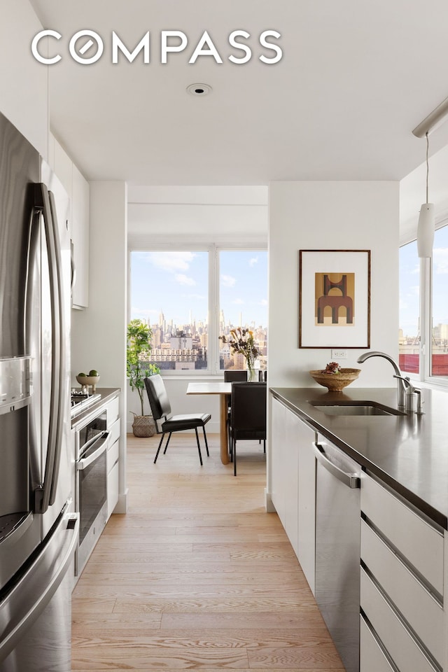 kitchen featuring a sink, dark countertops, appliances with stainless steel finishes, white cabinets, and light wood finished floors