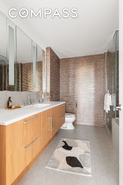 bathroom with a shower with door, tile walls, vanity, tile patterned floors, and toilet