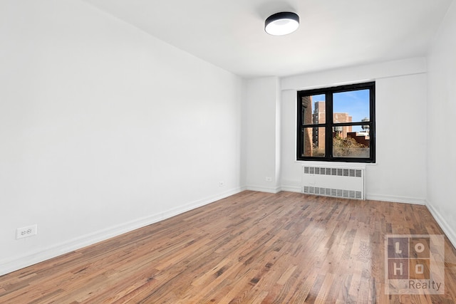 spare room with baseboards, wood finished floors, and radiator