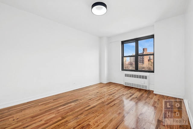 empty room with light wood-type flooring, baseboards, and radiator heating unit