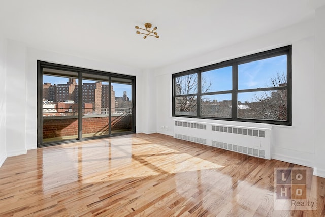 spare room with a view of city, radiator heating unit, wood finished floors, and baseboards