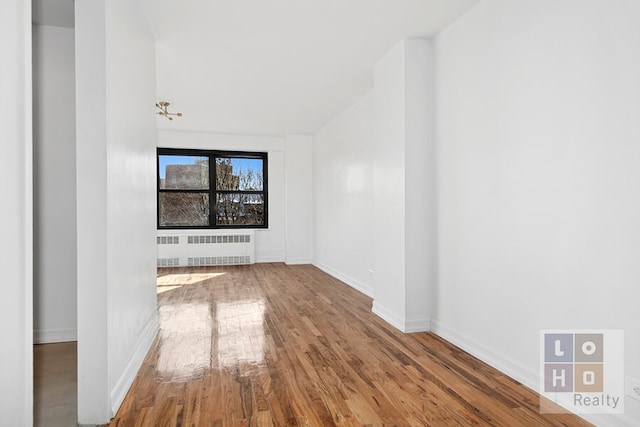 empty room featuring radiator heating unit, wood finished floors, and baseboards