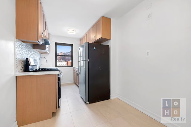 kitchen featuring light countertops, backsplash, appliances with stainless steel finishes, brown cabinetry, and baseboards