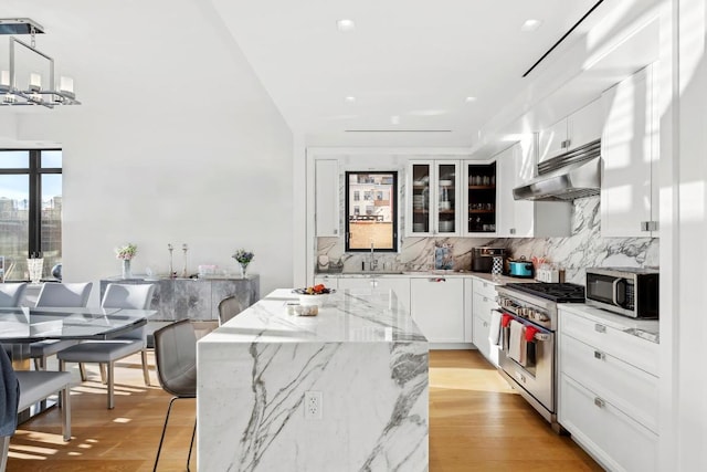 kitchen with appliances with stainless steel finishes, white cabinetry, decorative backsplash, hanging light fixtures, and a center island