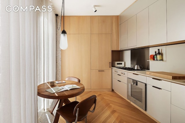 kitchen featuring wall oven, light brown cabinetry, hanging light fixtures, and light parquet floors