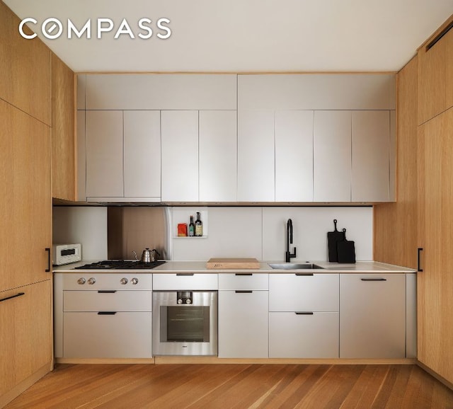 kitchen featuring appliances with stainless steel finishes, light brown cabinetry, light hardwood / wood-style floors, and sink