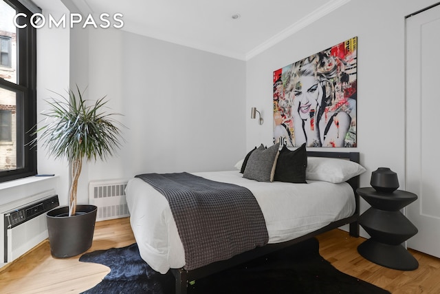 bedroom with wood finished floors, radiator heating unit, and crown molding