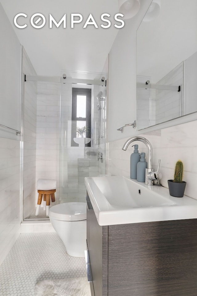 bathroom with toilet, vanity, a stall shower, tile patterned floors, and tile walls