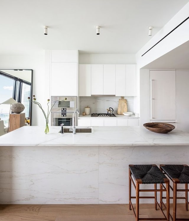 kitchen with tasteful backsplash, stainless steel gas stovetop, sink, a breakfast bar area, and white cabinets