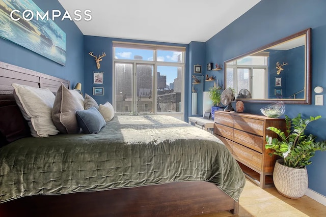 bedroom featuring a city view, multiple windows, wood finished floors, and baseboards