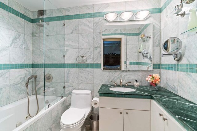 full bathroom featuring vanity, toilet, tiled shower / bath combo, and tile walls