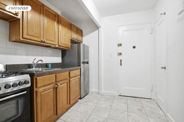 kitchen with light tile patterned floors, decorative backsplash, range with gas stovetop, brown cabinets, and a sink