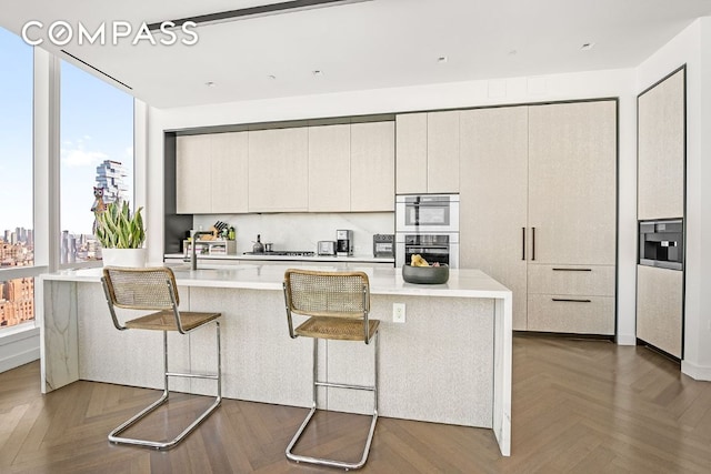 kitchen with tasteful backsplash, dark parquet flooring, an island with sink, and a kitchen bar