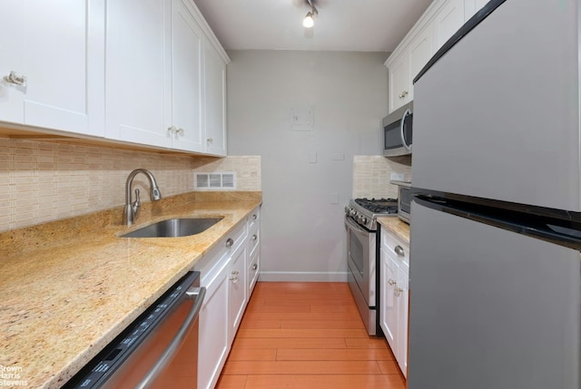 kitchen with sink, white cabinets, stainless steel appliances, light stone countertops, and backsplash