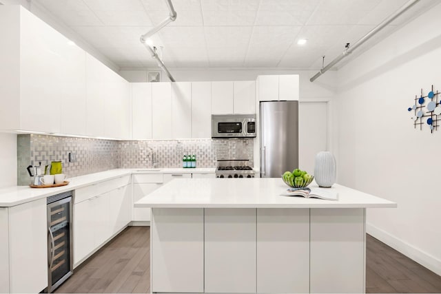 kitchen with beverage cooler, decorative backsplash, white cabinets, appliances with stainless steel finishes, and a center island