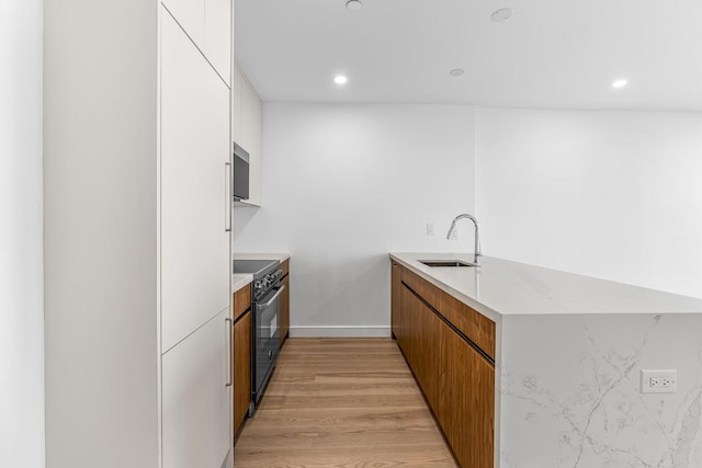 kitchen featuring white cabinetry, sink, stainless steel stove, and light hardwood / wood-style flooring