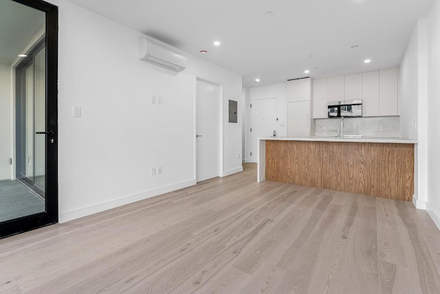 interior space with sink, light hardwood / wood-style flooring, a wall unit AC, electric panel, and white cabinets