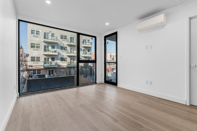 empty room featuring recessed lighting, light wood-style flooring, expansive windows, a wall mounted air conditioner, and baseboards