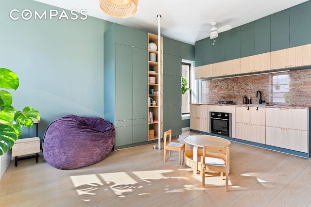 kitchen featuring a sink, black oven, light wood-type flooring, backsplash, and green cabinetry