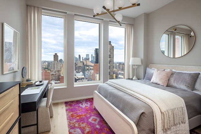 bedroom featuring wood finished floors, a notable chandelier, baseboards, and a city view
