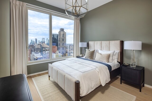bedroom with baseboards, a view of city, light wood-style flooring, and a chandelier