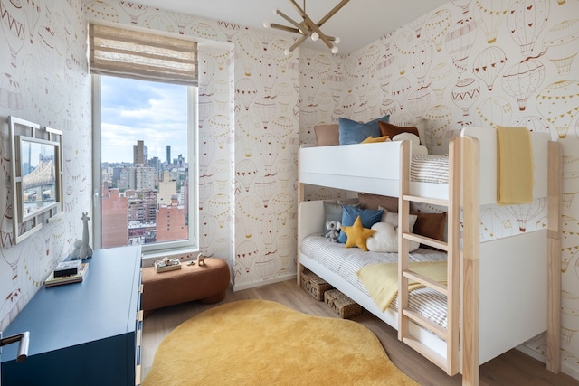 bedroom featuring a city view, wallpapered walls, and wood finished floors